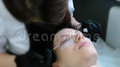 美容治疗。 美容师用刷子在卷发器睫毛上涂上一种溶液。 肉毒杆菌和睫毛层压